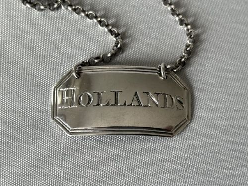 fig 1. An 18th-century octagonal silver decanter label engraved with HOLLANDS suspended by a silver chain.