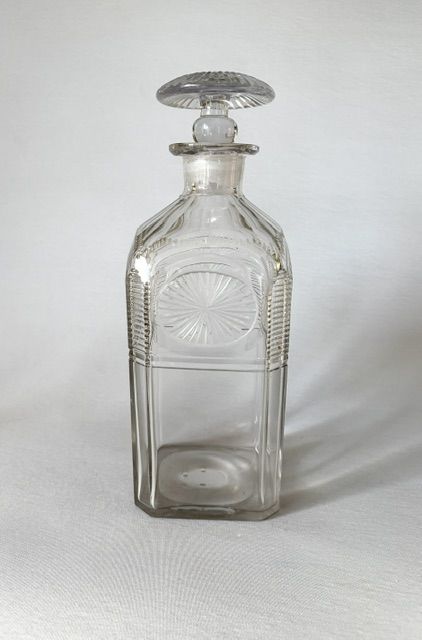 fig 1. A square clear cut glass decanter featuring wheel-cut starburst motifs, faceted shoulders, and a flat mushroom stopper.