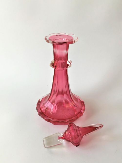 fig 1. A tall Victorian cranberry and clear cut glass cologne bottle featuring an elongated pointed spire stopper, faceted neck, and flared base.