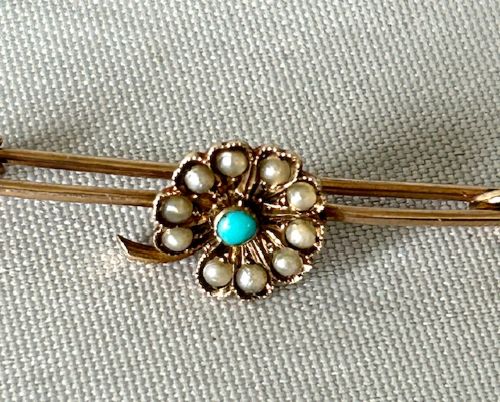 fig 1. A 9ct gold bar brooch featuring a central floral cluster motif set with a round turquoise cabochon encircled by seed pearls.