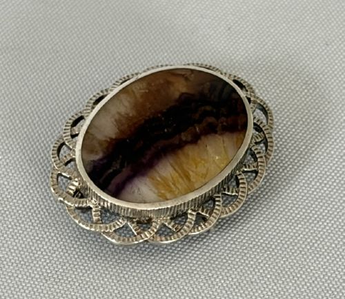 An oval Art Deco silver brooch featuring a polished Blue John stone with purple and yellow banding, encircled by a textured scalloped lattice border. View III