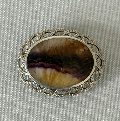 An oval Art Deco silver brooch featuring a polished Blue John stone with purple and yellow banding, encircled by a textured scalloped lattice border. View VII