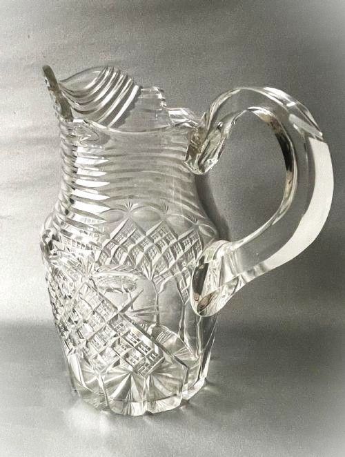 fig 1. A clear cut-glass water jug featuring a loop handle, horizontal step cuts around the neck, and diamond facets across the lower body.