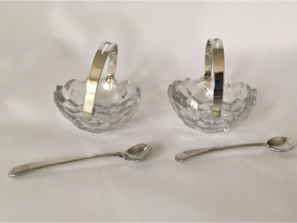 A pair of cut glass condiment baskets with silver spoons.