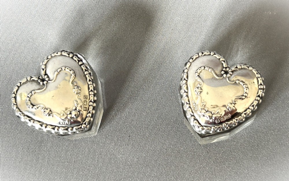 A pair of heart-shaped clear cut glass vanity jars featuring chased sterling silver lids with floral motifs. View II