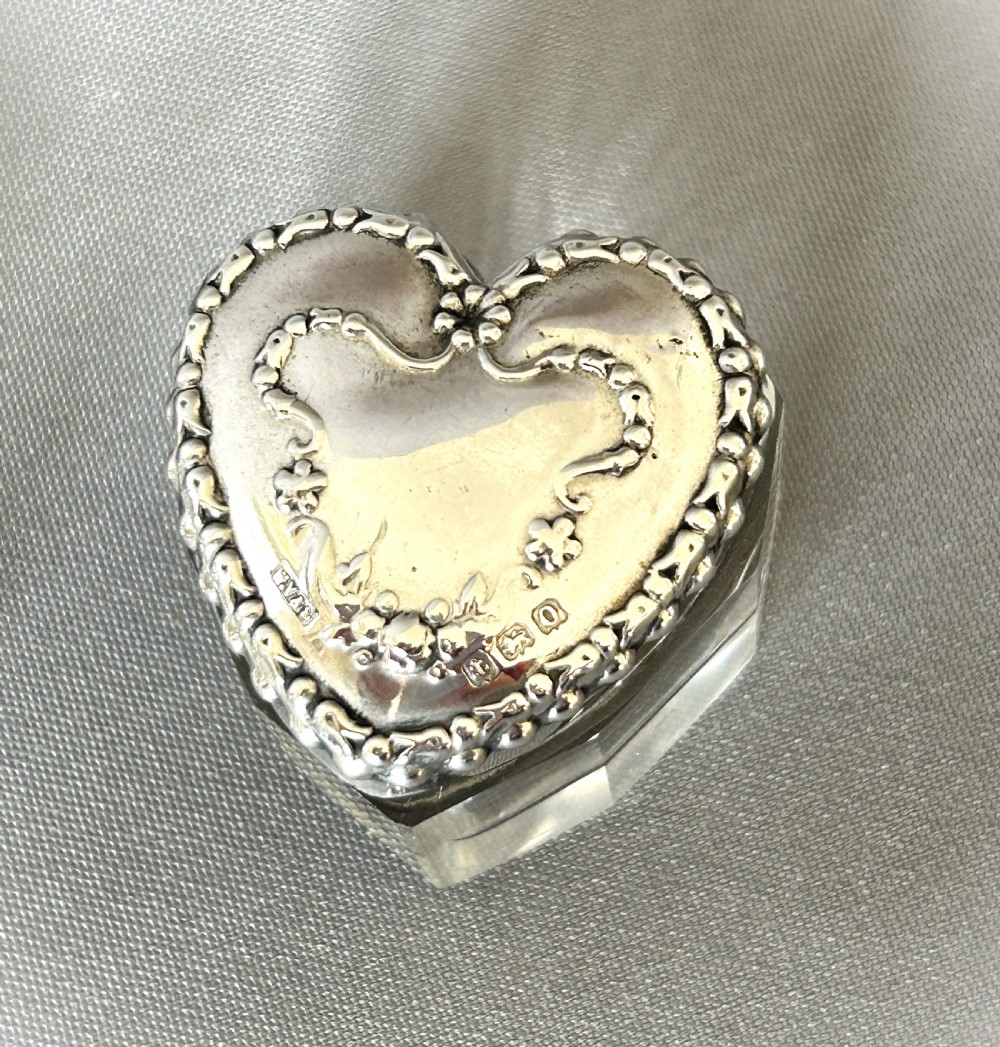 A pair of heart-shaped clear cut glass vanity jars featuring chased sterling silver lids with floral motifs. View III