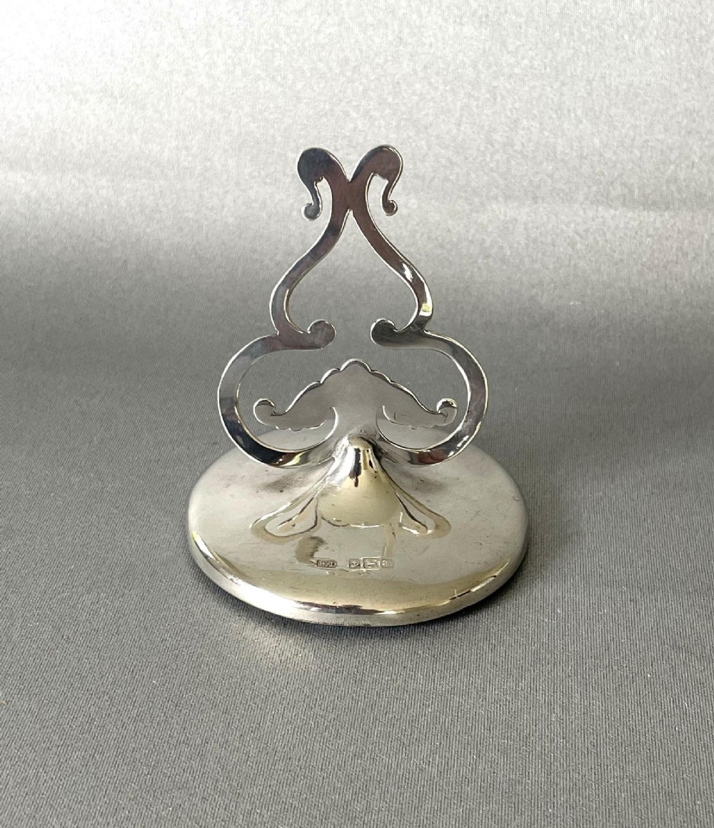 An Edwardian sterling silver menu card holder with an openwork scrollwork clip set upon a circular hallmarked base.