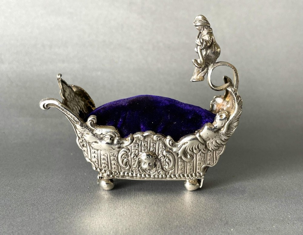 A Victorian silver novelty pin cushion shaped like an ornate sledge with a purple velvet cushion interior.