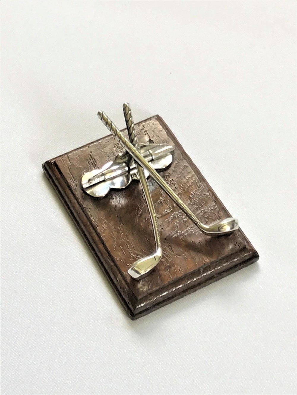 An Edwardian silver desk clip crafted in the shape of crossed golf clubs, mounted on a rectangular dark oak wood base.
