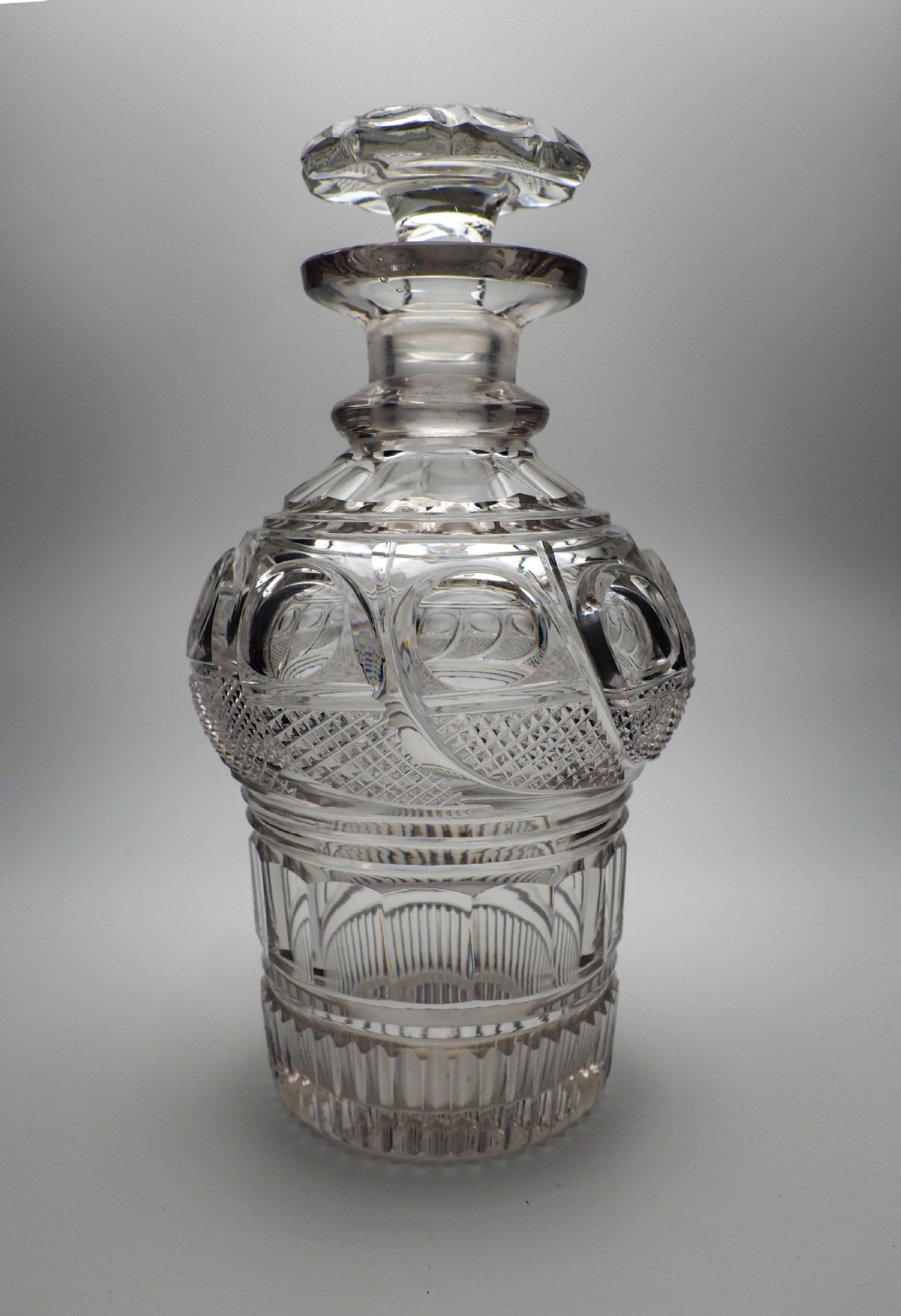 An Early Victorian clear cut glass spirit decanter featuring deep geometric cutting, a fluted base, and a flat faceted stopper.
