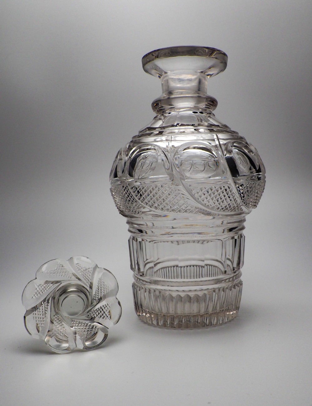An Early Victorian clear cut glass spirit decanter featuring deep geometric cutting, a fluted base, and a flat faceted stopper. View XII