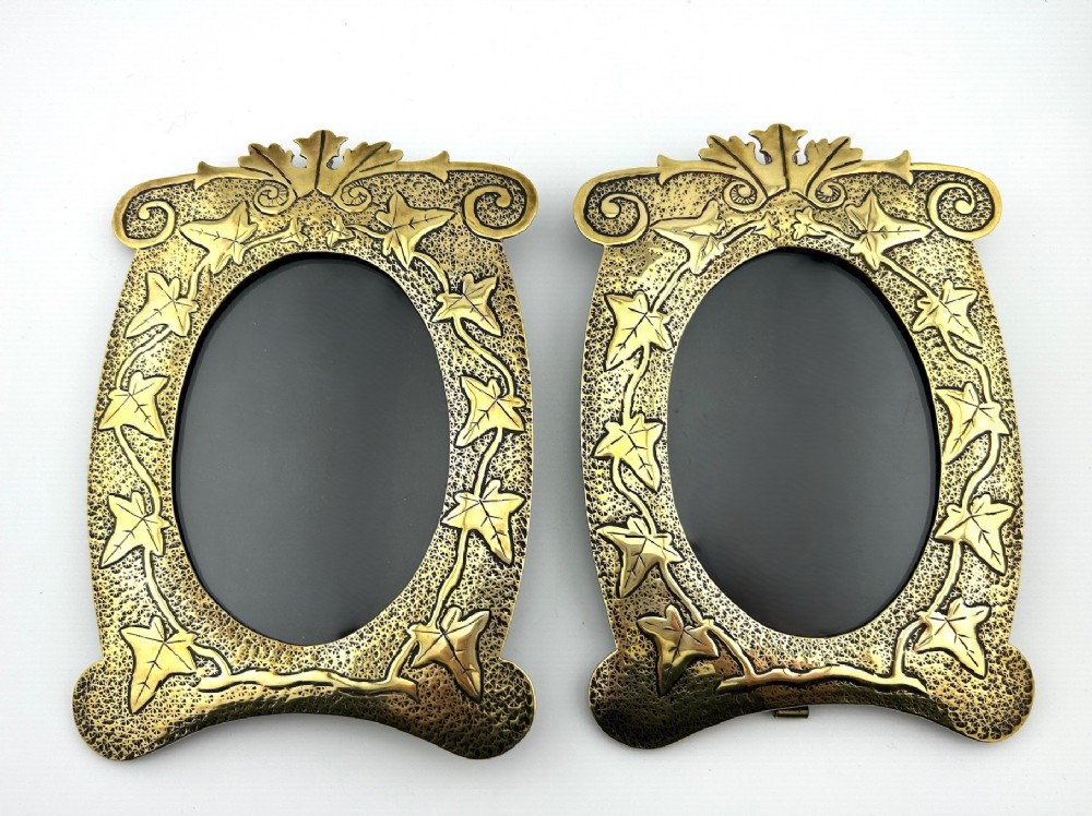 A pair of decorative brass picture frames featuring embossed ivy leaf motifs around oval openings against a stippled background.