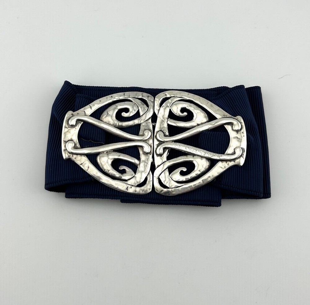 An Edwardian Arts and Crafts style two-part silver belt buckle featuring openwork scroll motifs and a hand-hammered finish set on a navy ribbon.