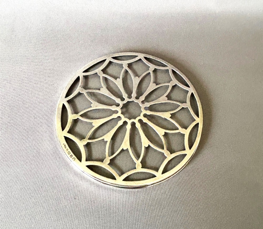 A circular Art Deco teapot stand featuring pierced silver lattice design mounted over a clear glass base.