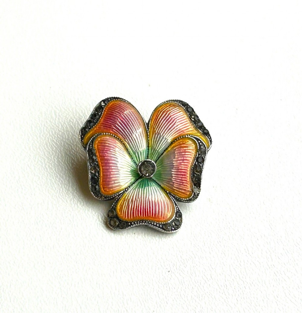An Edwardian flower-shaped silver brooch crafted with polychrome guilloche enamel in pink, orange, and green, surrounded by a marcasite border.
