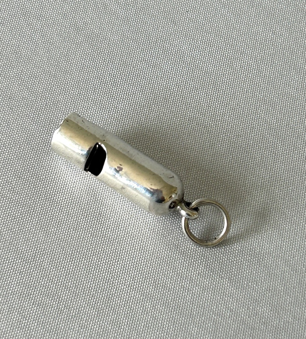 A small cylindrical Victorian silver dog whistle with a suspended loop ring attached to the rounded cap.