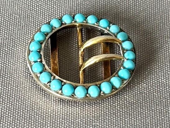 An oval silver gilt buckle framed with round turquoise cabochons and fitted with a central double prong mechanism.