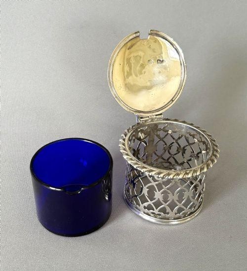 An early Victorian silver mustard pot with pierced fretwork sides, a cobalt blue glass liner, an engraved flat hinged lid, and a scroll handle. View II