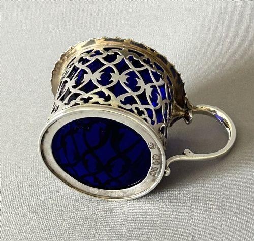 An early Victorian silver mustard pot with pierced fretwork sides, a cobalt blue glass liner, an engraved flat hinged lid, and a scroll handle. View III