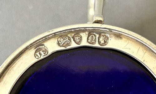 An early Victorian silver mustard pot with pierced fretwork sides, a cobalt blue glass liner, an engraved flat hinged lid, and a scroll handle. View V