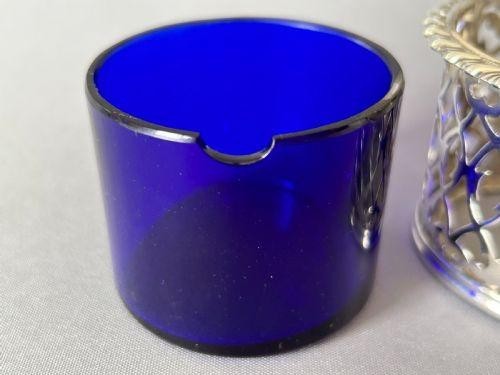 An early Victorian silver mustard pot with pierced fretwork sides, a cobalt blue glass liner, an engraved flat hinged lid, and a scroll handle. View VI