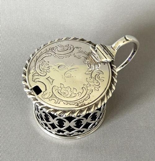 An early Victorian silver mustard pot with pierced fretwork sides, a cobalt blue glass liner, an engraved flat hinged lid, and a scroll handle. View VII