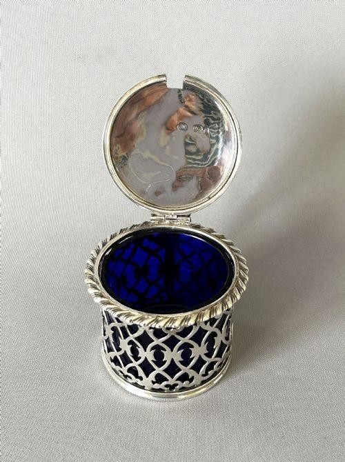 An early Victorian silver mustard pot with pierced fretwork sides, a cobalt blue glass liner, an engraved flat hinged lid, and a scroll handle. View VIII
