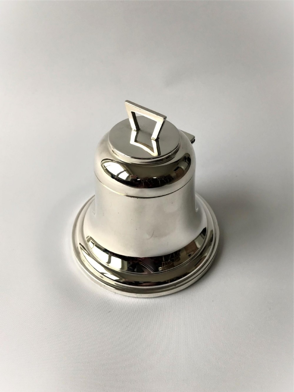 A polished George V silver novelty inkwell crafted in the shape of a bell with a hinged lid and flared base.