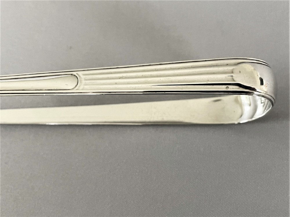 A pair of Georgian sterling silver sugar tongs featuring reeded arms and spoon grips on a grey textured background. View III
