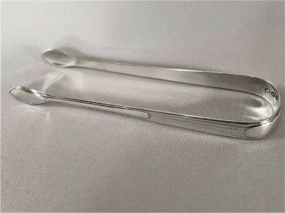 A pair of Georgian sterling silver sugar tongs featuring reeded arms and spoon grips on a grey textured background. View IV