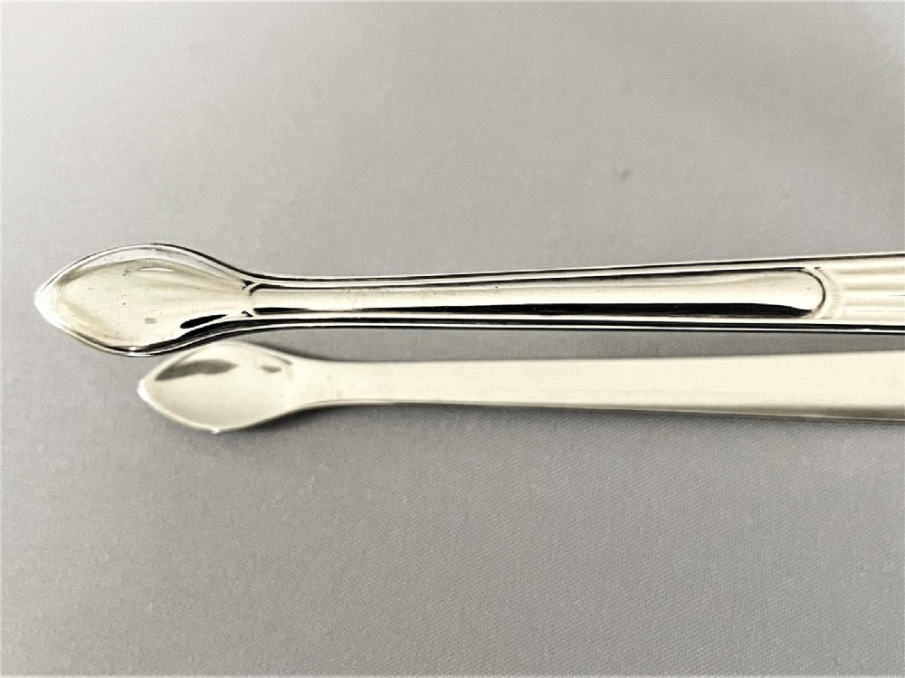 A pair of Georgian sterling silver sugar tongs featuring reeded arms and spoon grips on a grey textured background. View V