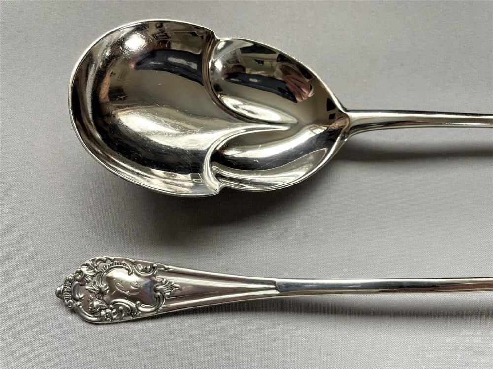 A pair of Edwardian silver salad servers consisting of a spoon and a fork with stylized leaf-shaped bowls and scroll-embossed handle terminals. View III