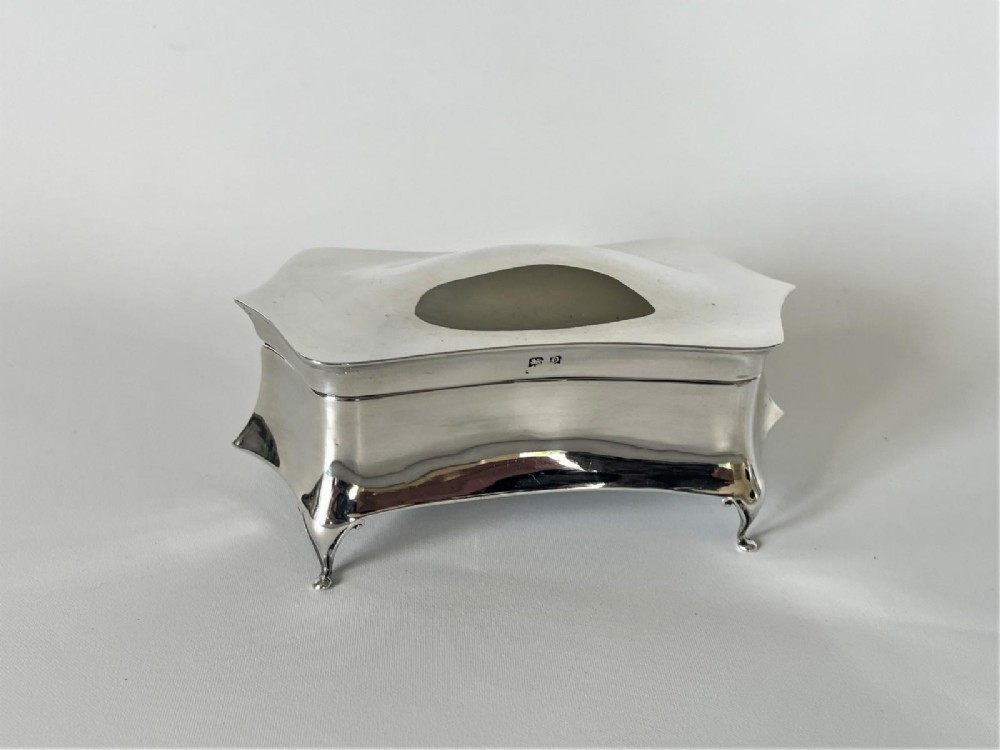 A polished George V sterling silver trinket box featuring a shaped flared body, hinged lid, and four cabriole legs.
