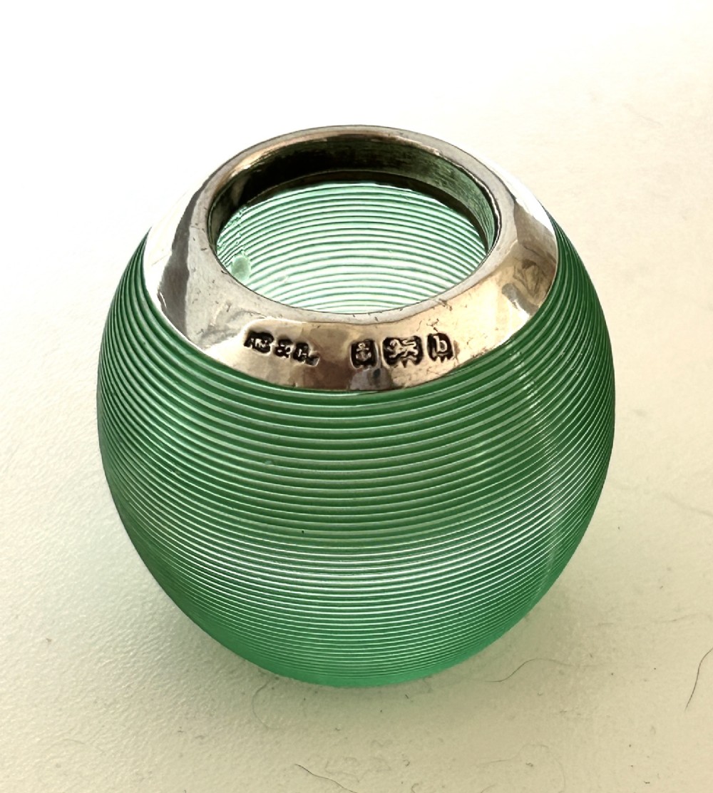 A spherical emerald green glass match striker featuring ribbed horizontal grooves and a hallmarked sterling silver collar at the rim.