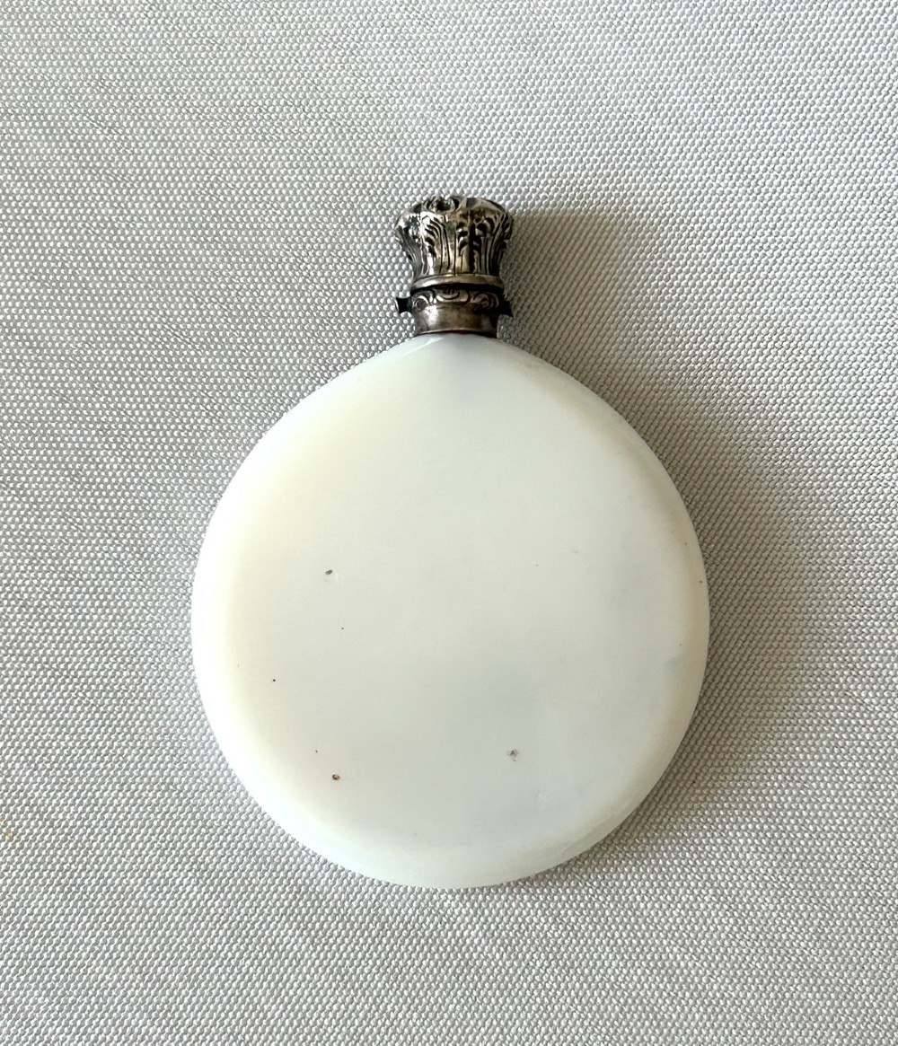 A circular white opaline glass scent bottle with a embossed silver cap top.