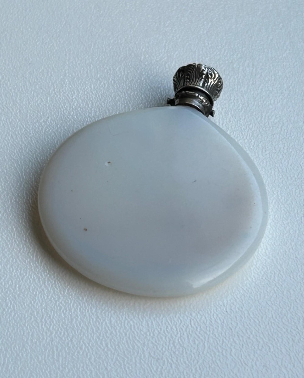 A circular white opaline glass scent bottle with a embossed silver cap top. View III