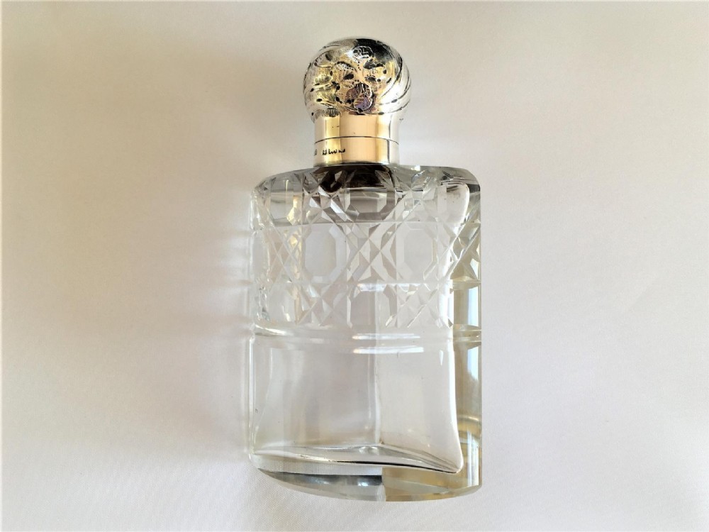 Three wedge-shaped clear glass cologne bottles with silver caps resting beside an open cylindrical black leather travel case. View V