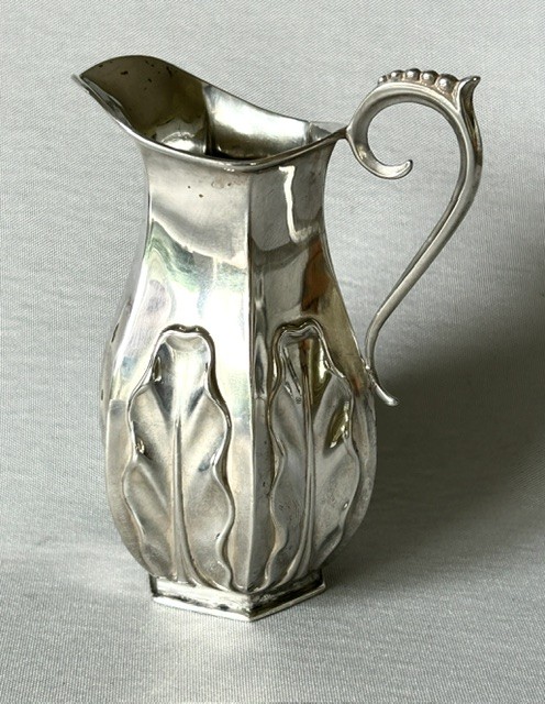 A late Victorian silver cream jug featuring embossed relief leaf motifs around its lower body and a beaded scroll handle.