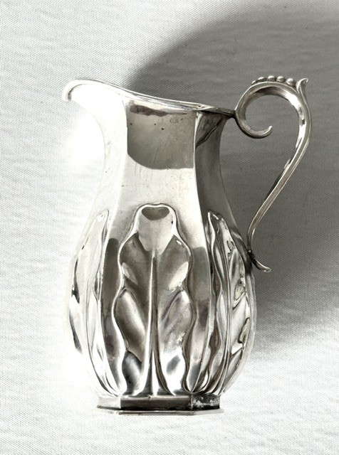 A late Victorian silver cream jug featuring embossed relief leaf motifs around its lower body and a beaded scroll handle. View III