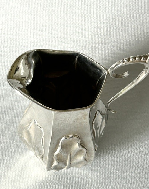 A late Victorian silver cream jug featuring embossed relief leaf motifs around its lower body and a beaded scroll handle. View VI