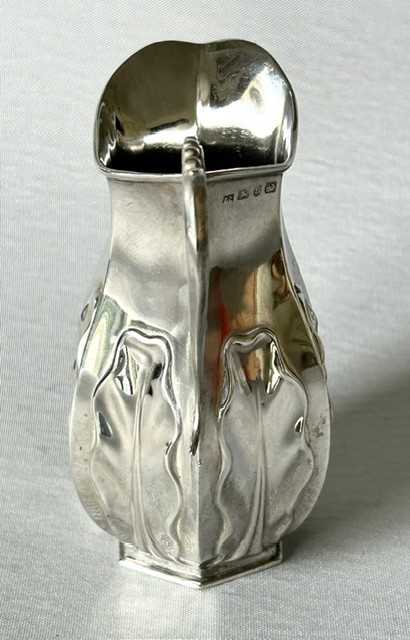 A late Victorian silver cream jug featuring embossed relief leaf motifs around its lower body and a beaded scroll handle. View VII