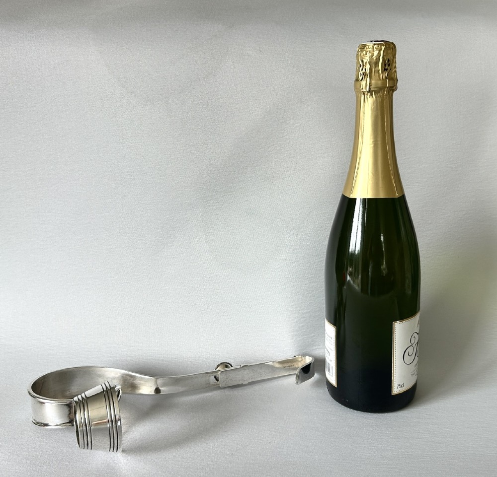 An Edwardian silver-plated champagne bottle holder featuring an adjustable collar mechanism and a curved pouring handle. View V