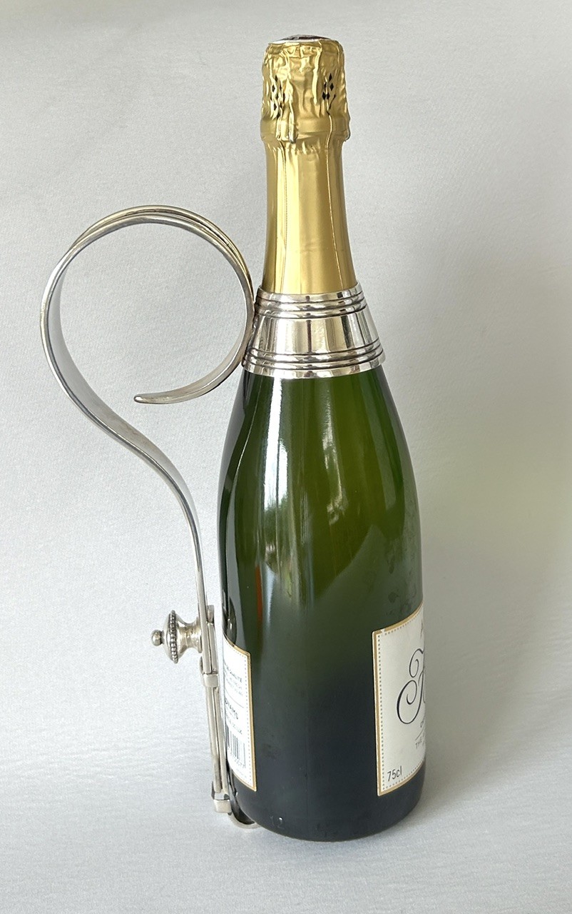 An Edwardian silver-plated champagne bottle holder featuring an adjustable collar mechanism and a curved pouring handle. View VI