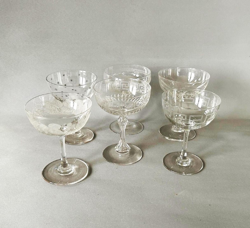 A harlequin set of six clear Victorian glass champagne coupes featuring varied etched motifs including starbursts and Greek key patterns.