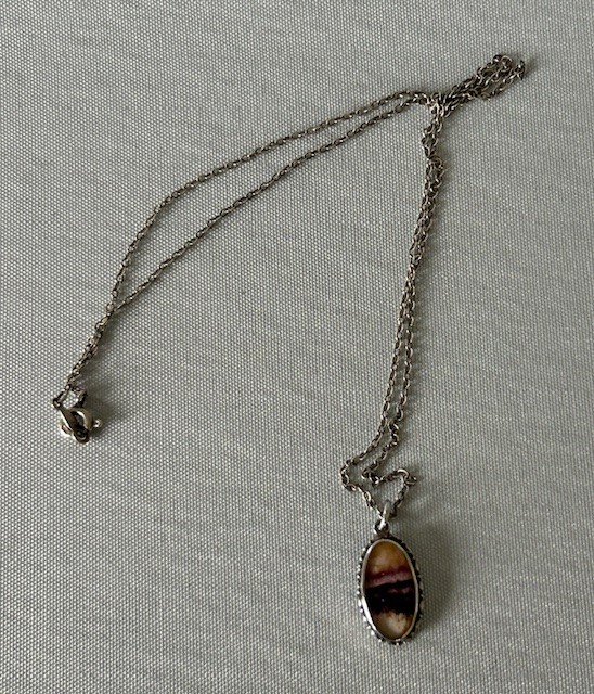 An oval Art Deco silver pendant featuring a banded purple and cream Blue John stone suspended from a silver trace chain. View II