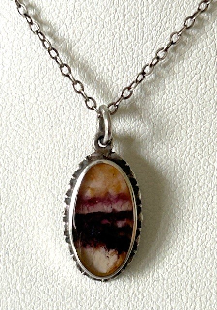 An oval Art Deco silver pendant featuring a banded purple and cream Blue John stone suspended from a silver trace chain. View V
