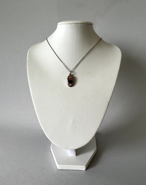 An oval Art Deco silver pendant featuring a banded purple and cream Blue John stone suspended from a silver trace chain. View VI
