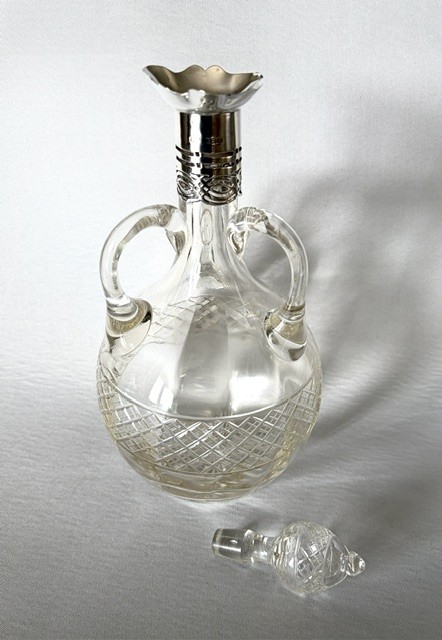 An Edwardian clear cut glass decanter featuring double scroll handles, a diamond-cut lower body, and a hallmarked silver collar topped with a faceted glass stopper. View III