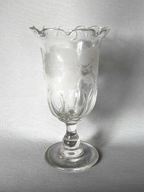 A clear glass Victorian celery vase featuring an etched floral pattern, a scalloped frilled rim, and a stemmed circular foot.