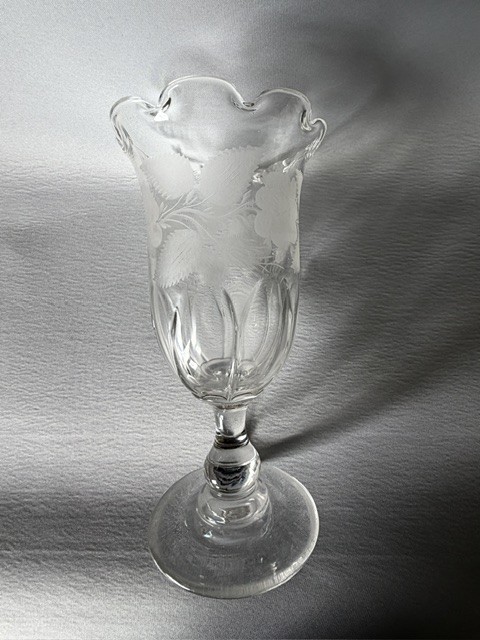 A clear glass Victorian celery vase featuring an etched floral pattern, a scalloped frilled rim, and a stemmed circular foot. View V
